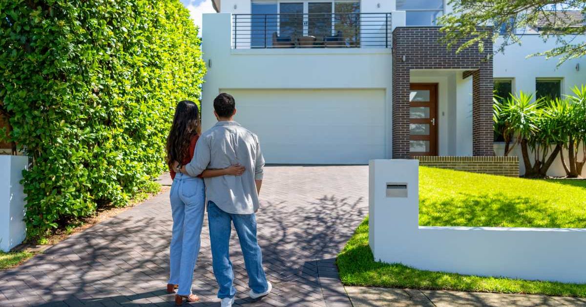 A happy couple standing in front of their new home. (Representative Cover Image Source: Getty Images |courtneyk)