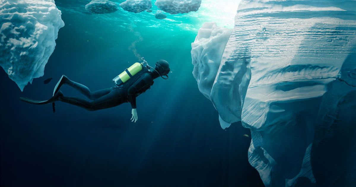 Diver inside icy, cool waters, swimming beneath a gigantic iceberg (Representative Cover Image Source: Getty Images | S_Bachstroem)