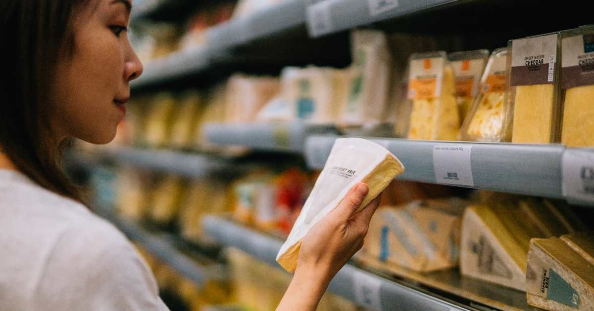 A woman is looking at a block of cheese in a grocery store. (Representative Cover Image Source: Oscar Wong)