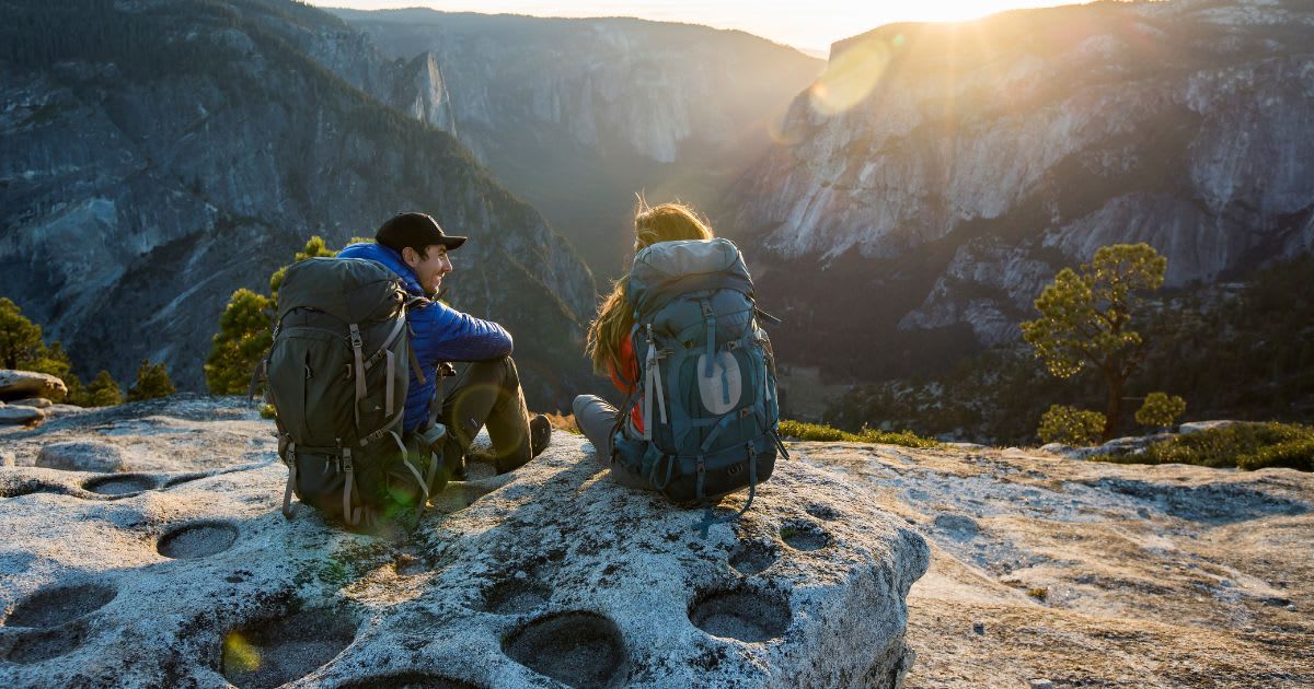 A couple sitting on a ledge while backpacking in Yosemite National Park (Representative Cover Image Source: Getty Images | Jordan Seimens)