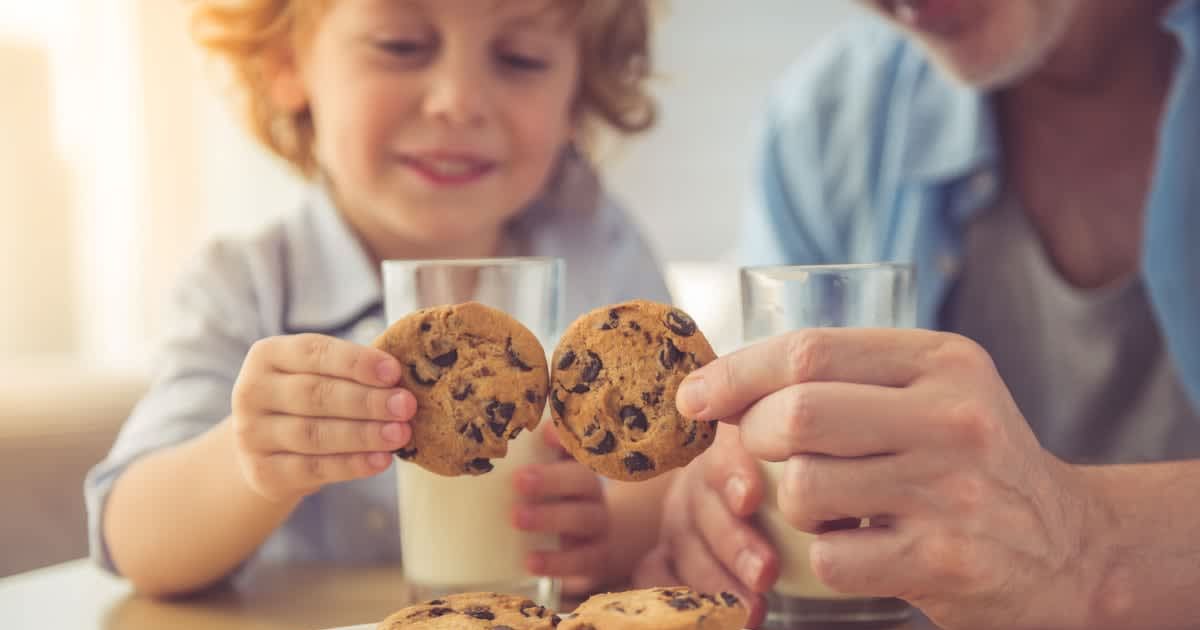 Parent and kid picking cookies from a plate while glasses of milk sit on the table. (Representative Cover Image Source: Getty Images | Vadimguzhva)