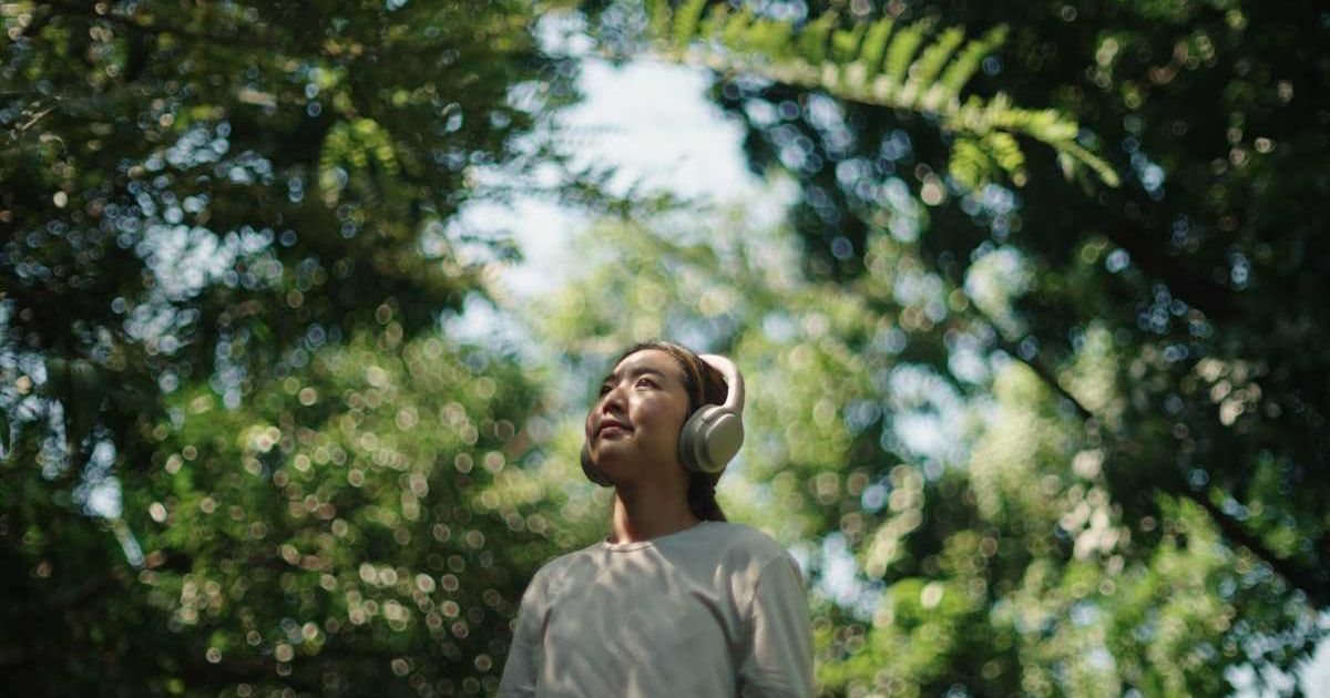 A woman wears headphones while relaxing in nature (Representative Cover Image Source: Getty Images | pocketlight)