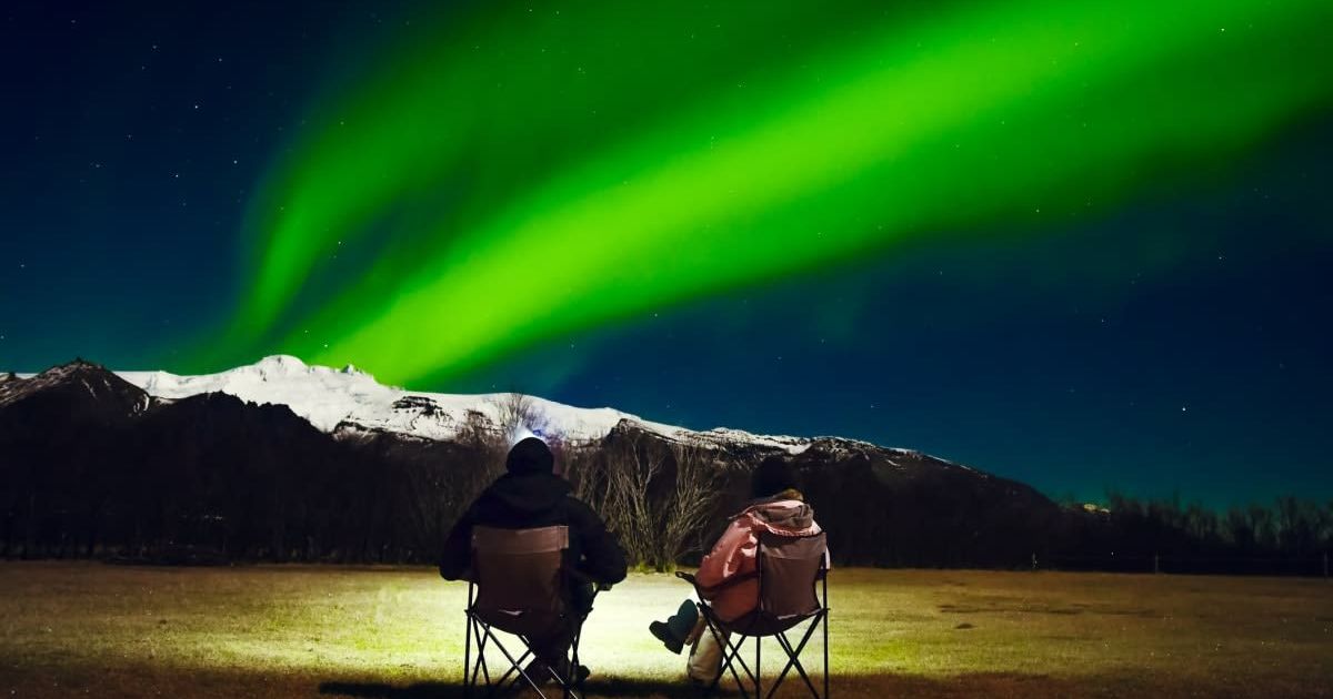A couple sits in foldable camping chairs, watching the Northern Lights (Representative Cover Image Source: Getty Images | EvaL)