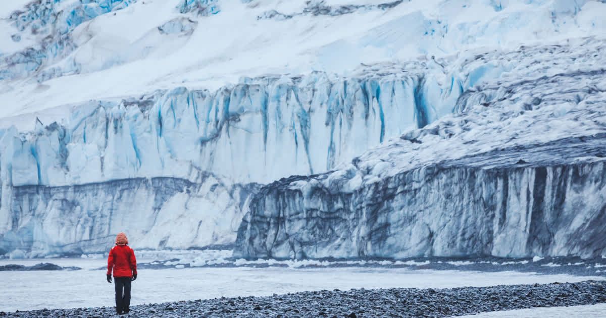 A man standing in front of a massive glacier. (Representative Cover Image Source: Getty Images | anyaberkut)