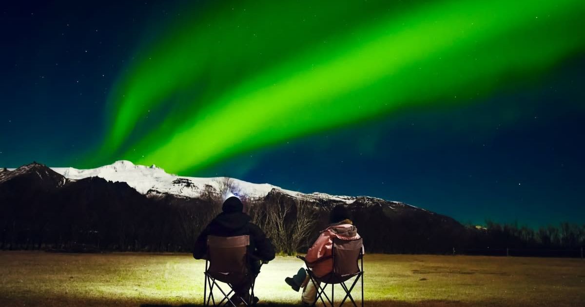 A couple sits in foldable camping chairs, watching the Northern Lights (Representative Cover Image Source: Getty Images | EvaL)