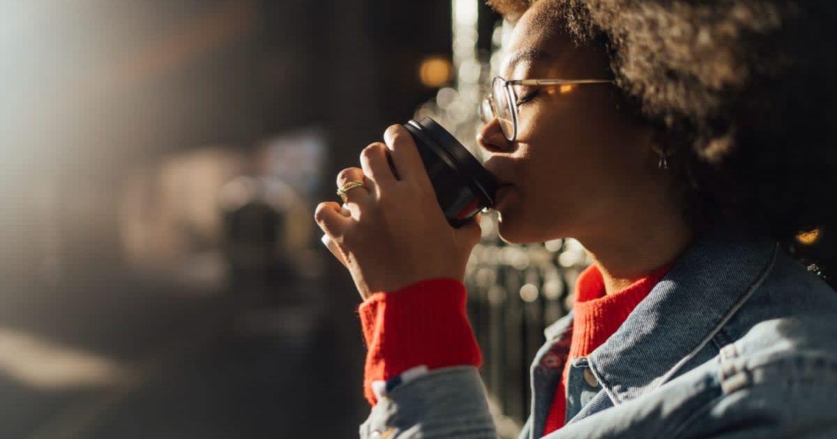  A young woman with eyes closed drinking coffee from a plastic to-go cup. (Representative Cover Image Source: Getty Images | Westend61)