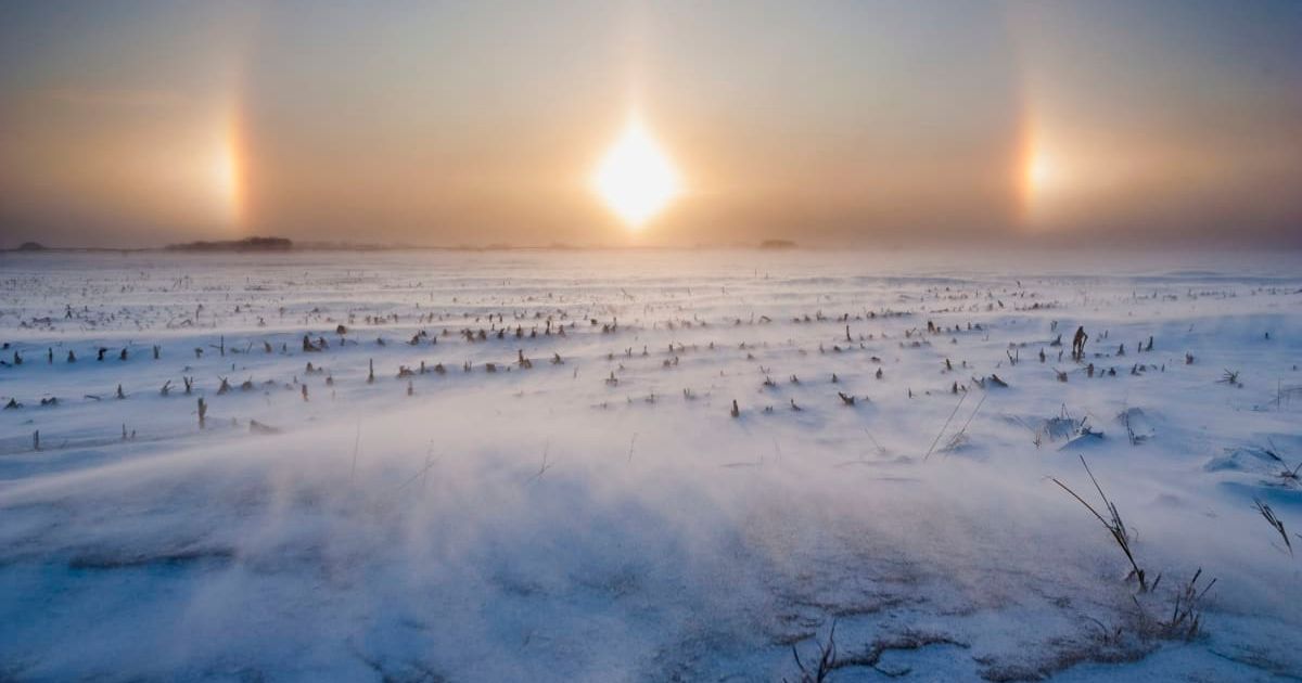 A white landscape blanketed in snow and a sundog, an optical phenomenon characterized by rainbowy patches of concentrated light (Representative Cover Image Source: Getty Images | Mike Hollingshead)