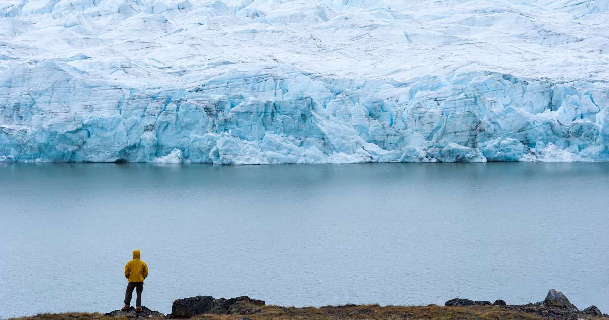 A hiker dwarfed by the fracture zone of a glacier on the Greenland Ice Sheet. (Representative Cover Image Source: Getty Images | Jason Edwards)